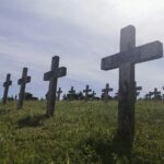 gray cross on green grass field under white clouds during daytime